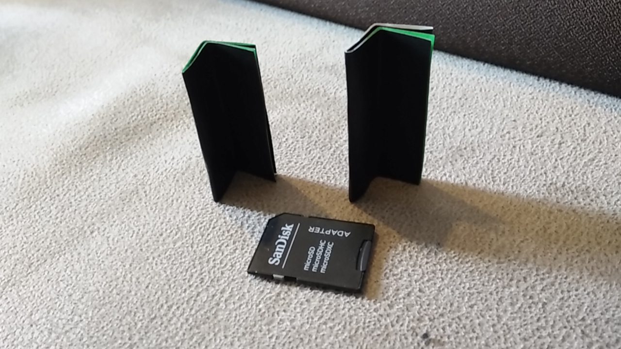 2 cardboard shims, pictured with an SD card for scale. The shims are about as wide as the SD card and twice as long, folded at 90 degrees along their length.